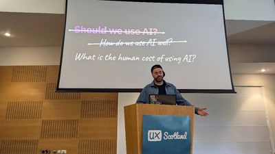 Craig gestures from the UX Scotland lectern beneath a slide that strikes through "Should we use AI?" and "How do we use AI well?" to ask "What is the human cost of using AI?".