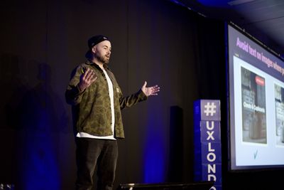 Craig gestures mid-talk on the blue-lit UX London stage, beside a slide advising "Avoid text on images" with e-commerce card examples.