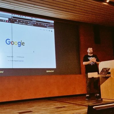 Craig presents beside a lectern, in front of a large projection of the Google Search home page.
