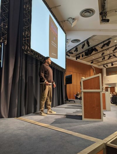 Craig on the Accessibility Scotland stage, presenting the cover of Sasha Costanza-Chock's book "Design Justice: community-led practices to build the worlds we need".