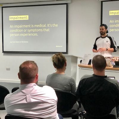 Craig gestures beside a slide reading "An impairment is medical. It's the condition or symptoms that person experiences", with the example "low vision or blindness".