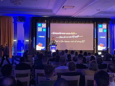 Craig addresses a full JSHeroes audience with a slide that crosses out "Should we use AI?" and "How do we use AI well?" to land on "What is the human cost of using AI?".