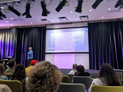 Craig on the purple-lit stage at Access Given, presenting a line chart showing how AI agent accuracy falls as the number of steps increases, credited to Utkarsh Kanwat.