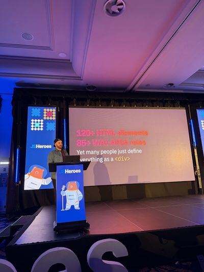 Craig presents at the JSHeroes lectern beneath a slide reading "120+ HTML elements, 85+ WAI-ARIA roles — yet many people just define everything as a div".