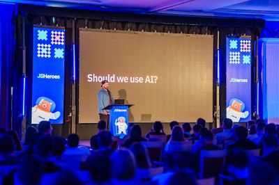 Craig opens his JSHeroes talk from the branded lectern, facing a huge screen asking "Should we use AI?" in front of a packed ballroom.