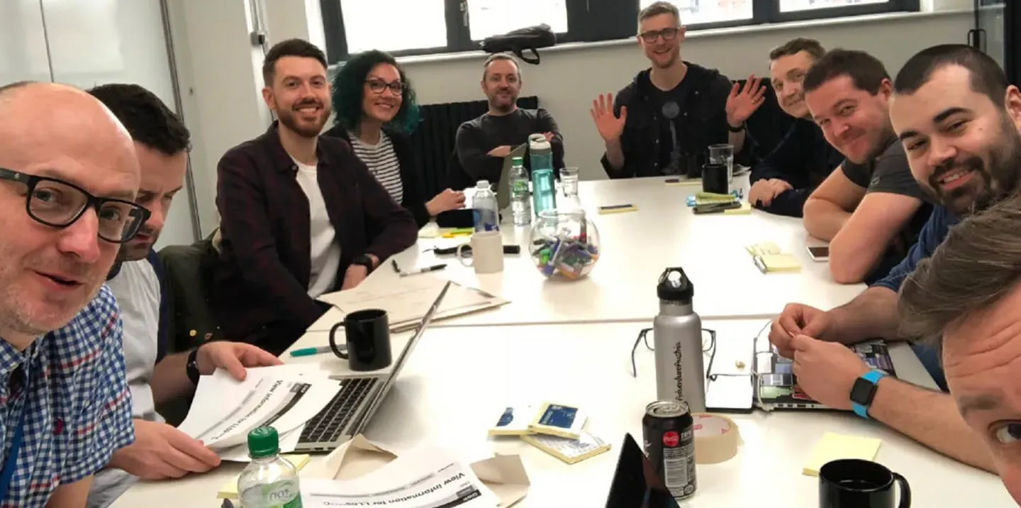 A group of 10 designers sat around a table waving at the camera.